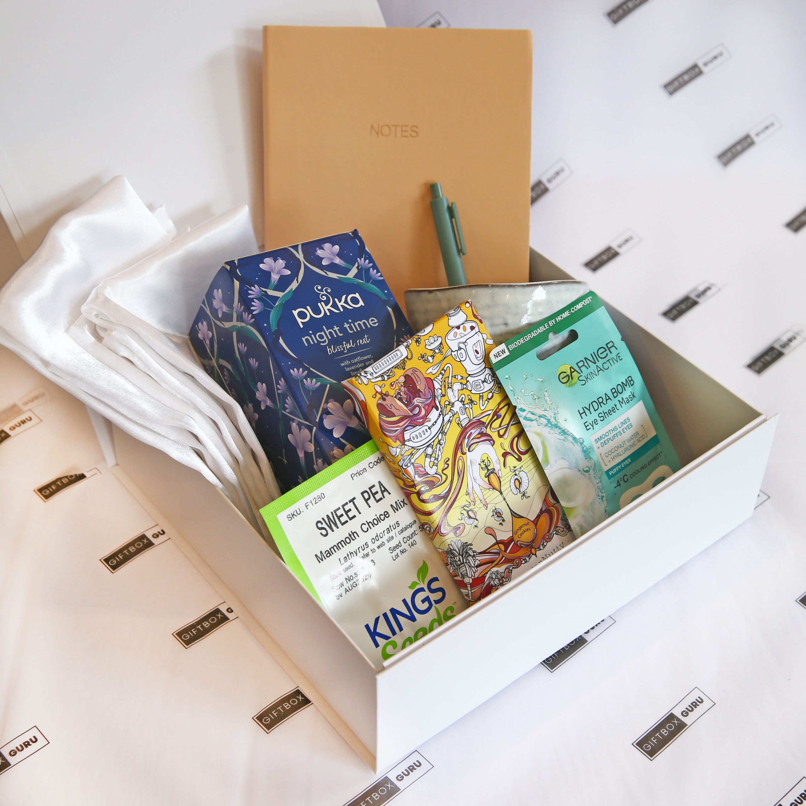 gift box with tea, white satin pillow cases, chocolate, flower seeds, eye mask, notebook and pen