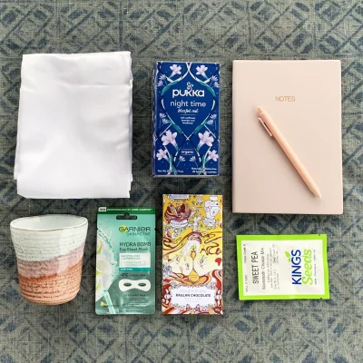 A giftbox for someone who has been dumped including white satin pillow cases, a box of herbal tea, note book and pen, tea cup, flower seeds, an eye mask and a small block of chocolate