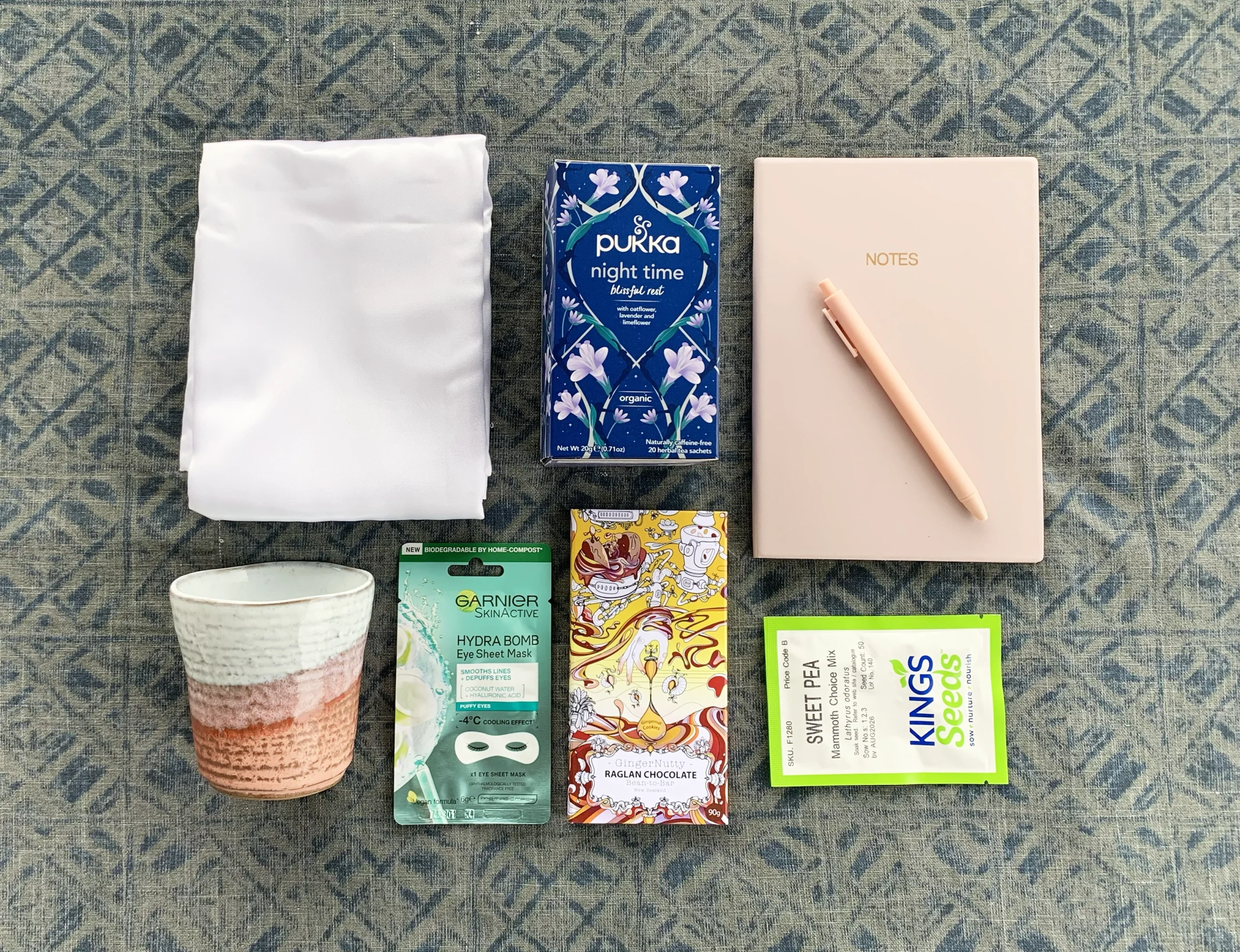 A giftbox for someone who has been dumped including white satin pillow cases, a box of herbal tea, note book and pen, tea cup, flower seeds, an eye mask and a small block of chocolate