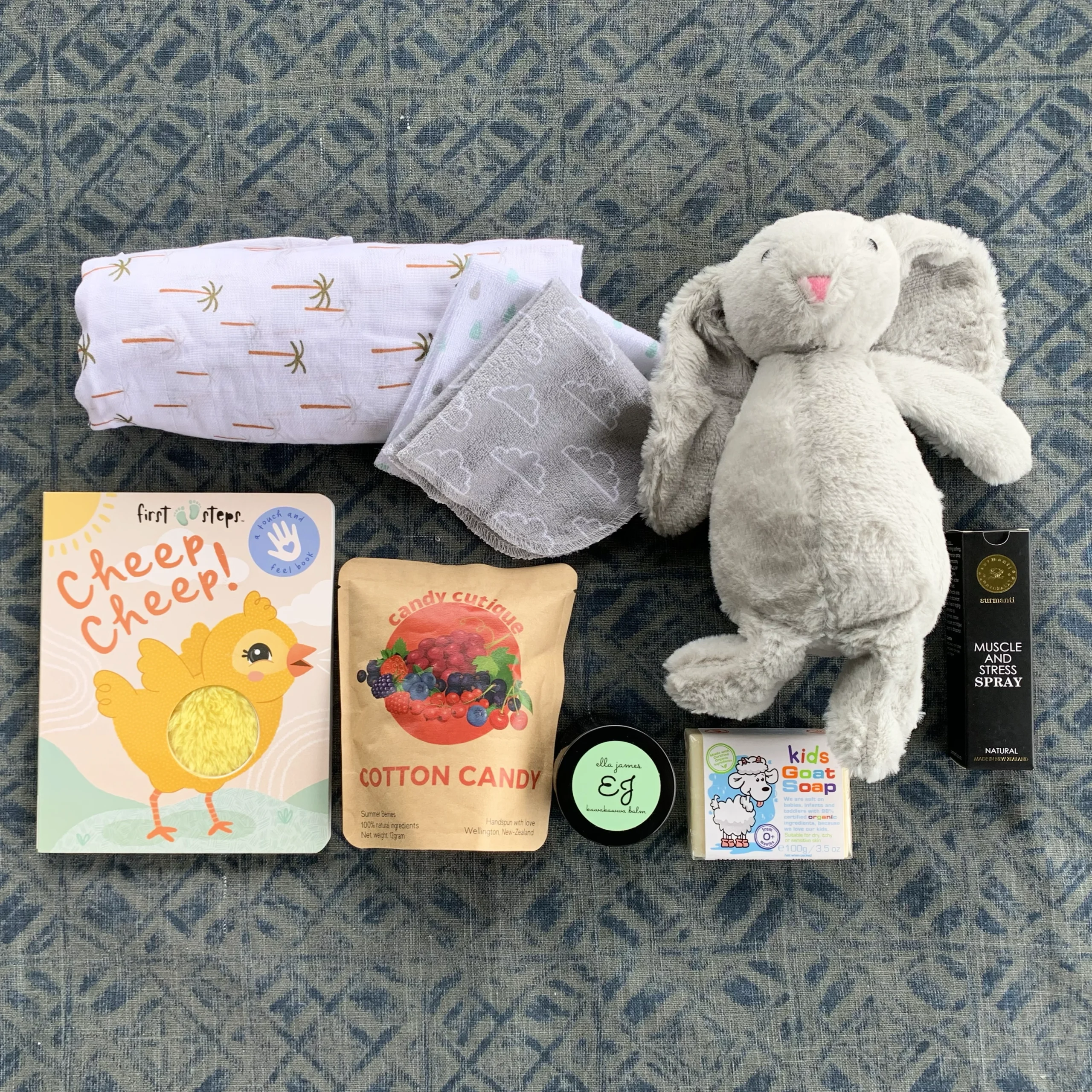 New baby gift box containing a baby book, candy floss, a jar of kawakawa balm, a rabbit soft toy, soap and a baby wrap