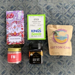 Tiny Token Gift Box includes a block of dark chocolate, cocktail rim duster in a jar, a jar of honey, a packet of flower seeds and a packet of cotton candy.