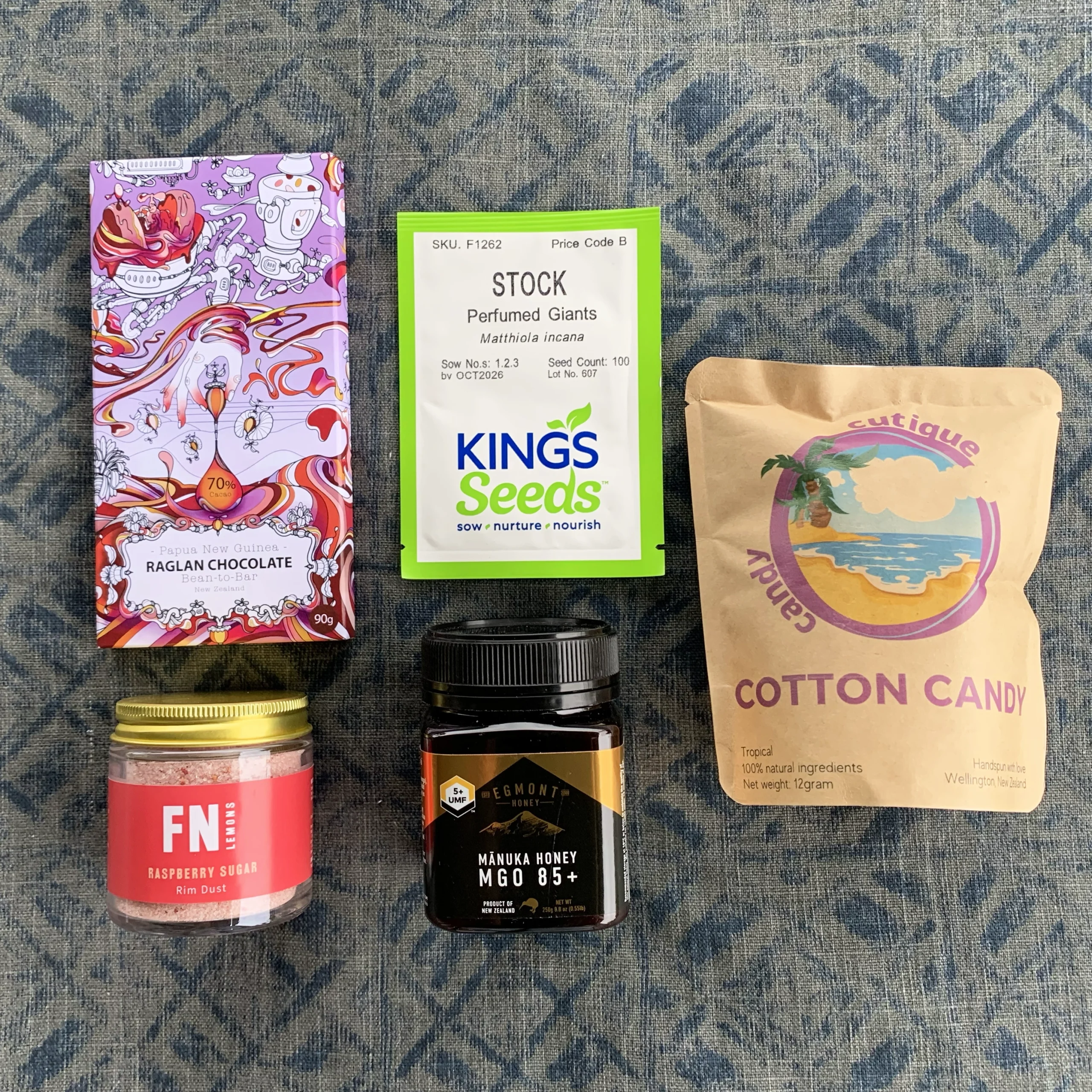 Tiny Token Gift Box includes a block of dark chocolate, cocktail rim duster in a jar, a jar of honey, a packet of flower seeds and a packet of cotton candy.